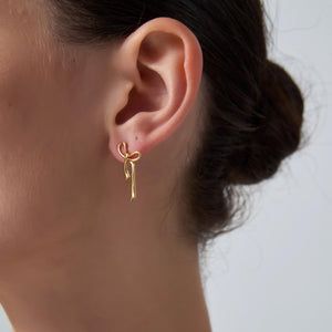 Gold bow-shaped earring worn on a person's ear with a neutral background