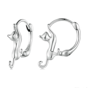 A collection of cat-shaped huggie hoop earrings in various metal finishes, displayed against a blue background.