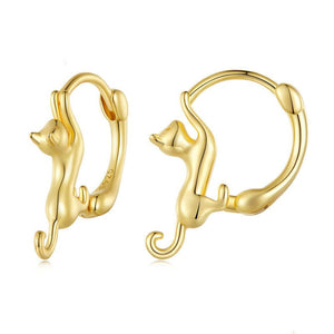A collection of cat-shaped huggie hoop earrings in various metal finishes, displayed against a blue background.