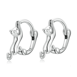 A collection of cat-shaped huggie hoop earrings in various metal finishes, displayed against a blue background.