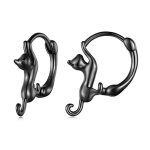 A collection of cat-shaped huggie hoop earrings in various metal finishes, displayed against a blue background.