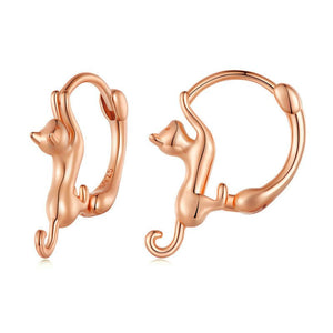 A collection of cat-shaped huggie hoop earrings in various metal finishes, displayed against a blue background.