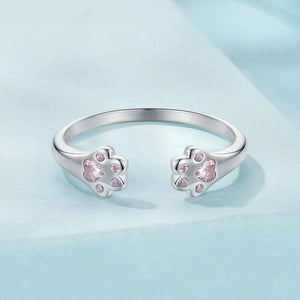 Silver ring with paw-shaped pink gemstones on a light blue background