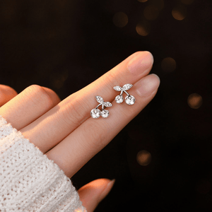 Silver earrings held on a hand against a dark background