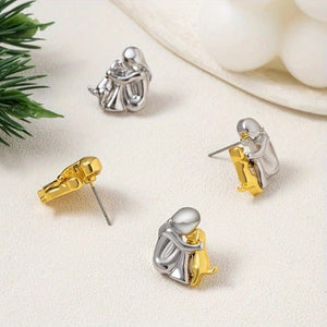 Pair of gold and silver earrings on a light surface with greenery.