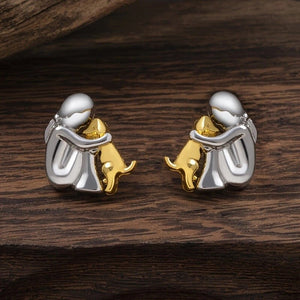 Pair of earrings featuring a silver figure with a gold dog on a wooden surface