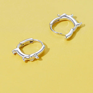 A pair of sterling silver hoop earrings with a dachshund dog design, displayed against a yellow background.