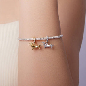 A bracelet with two dachshund charms on a wrist against a neutral background