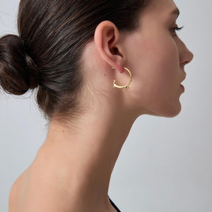 Woman wearing a gold hoop earring on a plain background