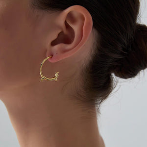 Gold hoop earring worn by a person with a neutral background