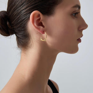 Close-up of a woman wearing a gold hoop earring against a neutral background