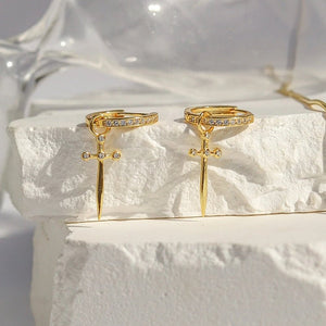 Gold earrings with cross design on a textured white surface