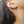 Close-up of an ear wearing silver hoop earrings with a cross charm and chain.