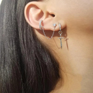 Close-up of an ear wearing silver hoop earrings with a cross charm and chain.