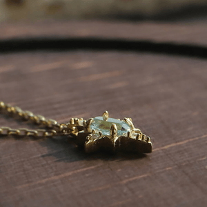 Gold necklace with a green gemstone pendant on a wooden surface