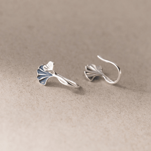 Pair of silver ginkgo leaf earrings on a beige background