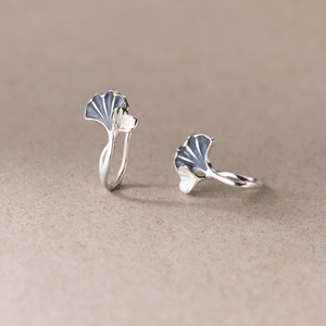 Pair of silver ginkgo leaf earrings on a beige background