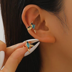 Close-up of an ear with a gold earring featuring blue gemstones, held by a hand.