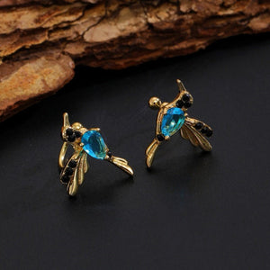 Gold bee-shaped earrings with blue gemstones on a dark surface
