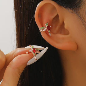 Close-up of a person wearing a silver earring with red and green gemstones, holding another similar earring.