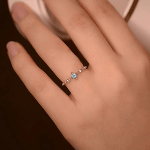 Close-up of a hand wearing a ring with a blue gemstone on a dark background
