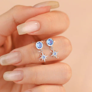 Earrings with blue gemstones held between fingers against a beige background