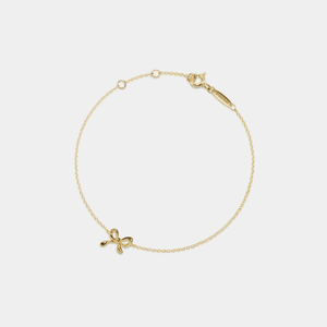 Gold bracelet with a bow-shaped charm on a light gray background