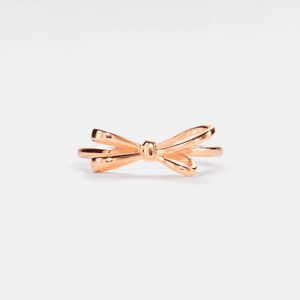 A gold-colored bow tie stacking band ring on a white background