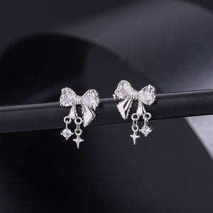 Silver bow-shaped earrings with star charms on a dark background