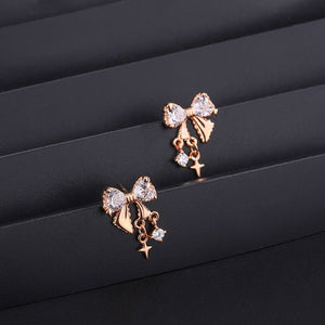 Rose gold bow-shaped earrings with clear stones on a black surface