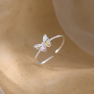 Silver butterfly ring with colored gemstones on a beige surface