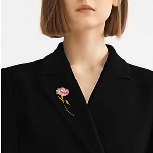 Person wearing a black blazer with a pink floral brooch on a plain background