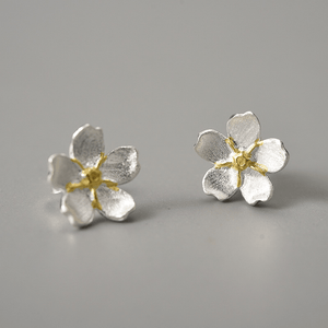 Silver flower-shaped earrings with gold centers on a gray background