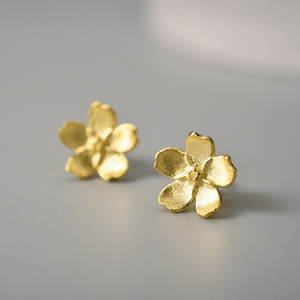 Gold flower-shaped earrings on a gray background