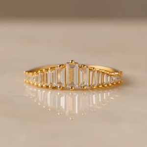 Gold ring with emerald-cut diamonds on a beige background