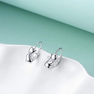A pair of sterling silver hoop earrings with a cat face design, placed against a blue and white background.