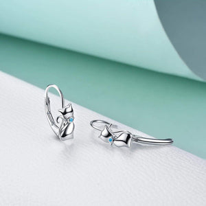 A pair of sterling silver hoop earrings with a cat face design, placed against a blue and white background.