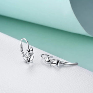 Silver cat-shaped earrings on a light green and white background