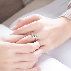 Close-up of a hand wearing a silver ring with a diamond on a neutral background