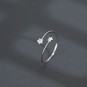Silver open ring with star and flower designs on a dark gray background