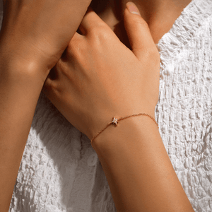 Close-up of a hand wearing a gold bracelet with a star charm on a textured white fabric background.