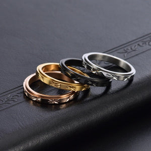 Four rings in gold, rose gold, black, and silver on a dark textured surface