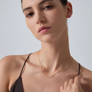 Woman wearing a gold necklace against a plain background