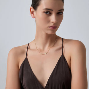 Woman wearing a brown strappy top and gold necklace against a light gray background