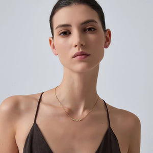 Woman wearing a delicate gold necklace against a plain background