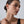 Close-up of a woman wearing a delicate earring against a neutral background