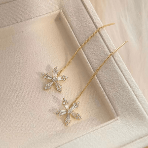 Gold cross-shaped earrings on a soft beige fabric background