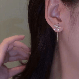 Close-up of a woman wearing a floral earring with a dangling chain.