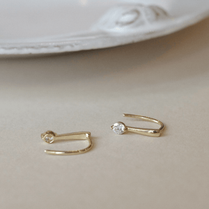 A pair of small gold-colored huggie hoop earrings with a geometric design, displayed on a white surface.