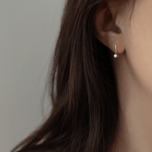 Close-up of an ear wearing a gold earring with a green gemstone against a neutral background
